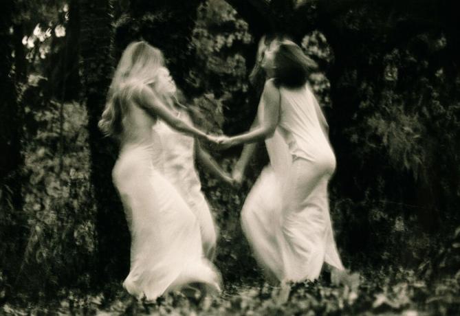 Fire unge kvinder danser i skoven og holder hænderne (sort / hvid, sløret bevægelse)