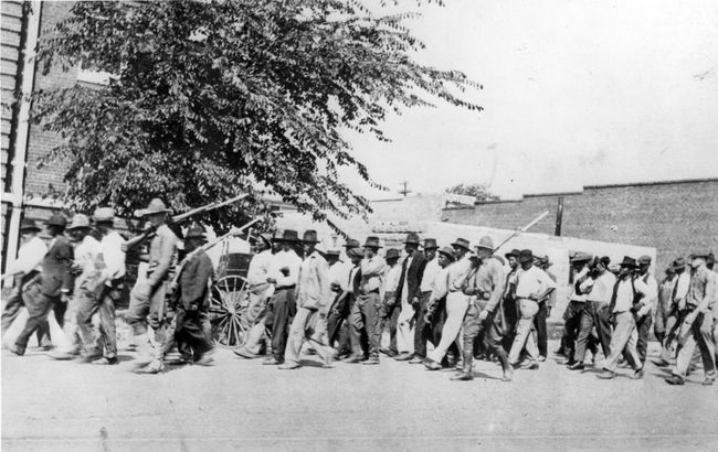 En gruppe nationalgarde-tropper, der bærer rifler med påsatte bajonetter, eskorterer ubevæbnede sorte mænd til et interneringscenter efter Tulsa Race Massacre, Tulsa, Oklahoma, juni 1921.