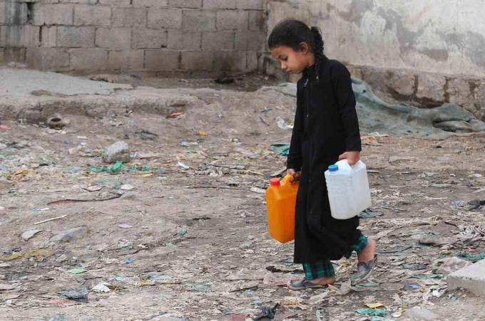 En lille pige bærer jerrycans fyldt med rent vand fra en velgørenhedspumpe under en fortsat krise med rent vand i Yemen