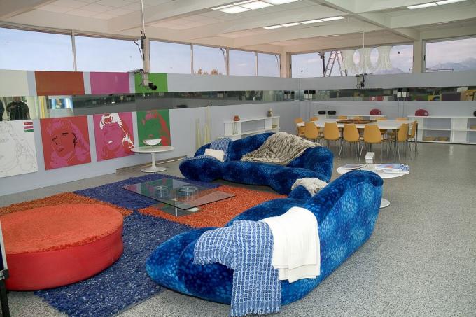 åbent rum med præstervinduer og spejle, blå sofa ved siden af ​​røde cirkulære sofa, bord og stole i baggrunden