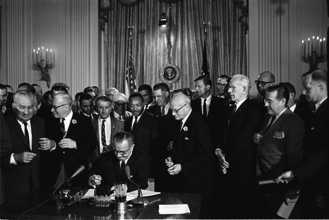 Præsident Lyndon B. Johnson underskriver 1964 Civil Rights Act, mens Martin Luther King, Jr., og andre, ser på.