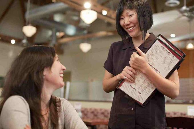 En servitrice med menuer i hånden og taler med en kunde.