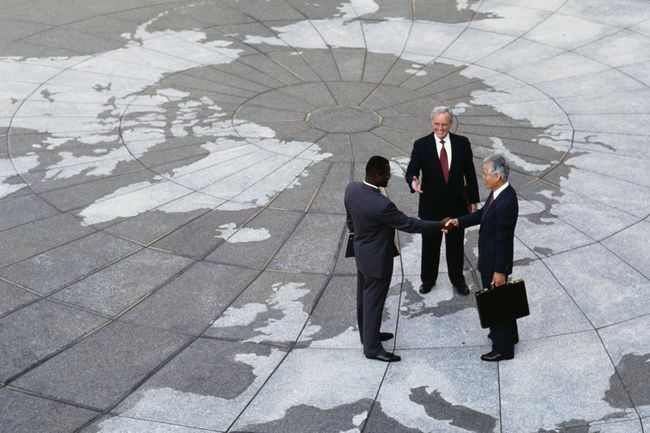  Økonomisk regionalisme: Forretningsmænd giver hånd på kort over jordkloden.