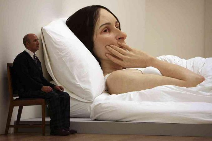 En mand sidder ved siden af ​​en enorm skulptur af en døende kvinde
