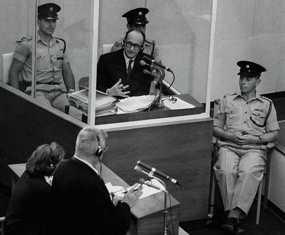 Den nazistiske krigsforbryder Adolph Eichmann står i en beskyttelsesglasboks flankeret af det israelske politi under hans retssag den 22. juni 1961 i Jerusalem.